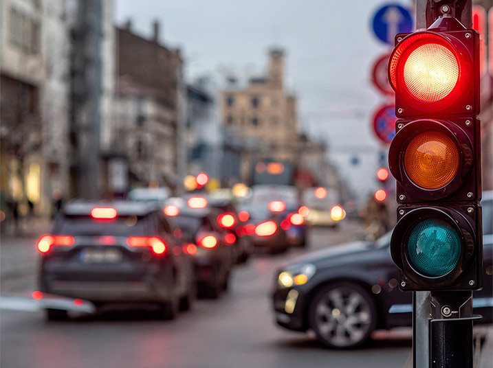 Traffic stopped at a red light on a busy city street, with cars and buildings blurred in the background.